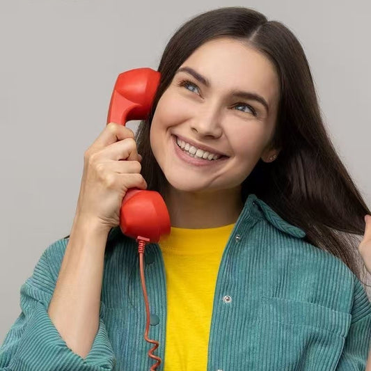 Smiling woman holding a red phone while wearing a green shirt and yellow t-shirt, looking happy.