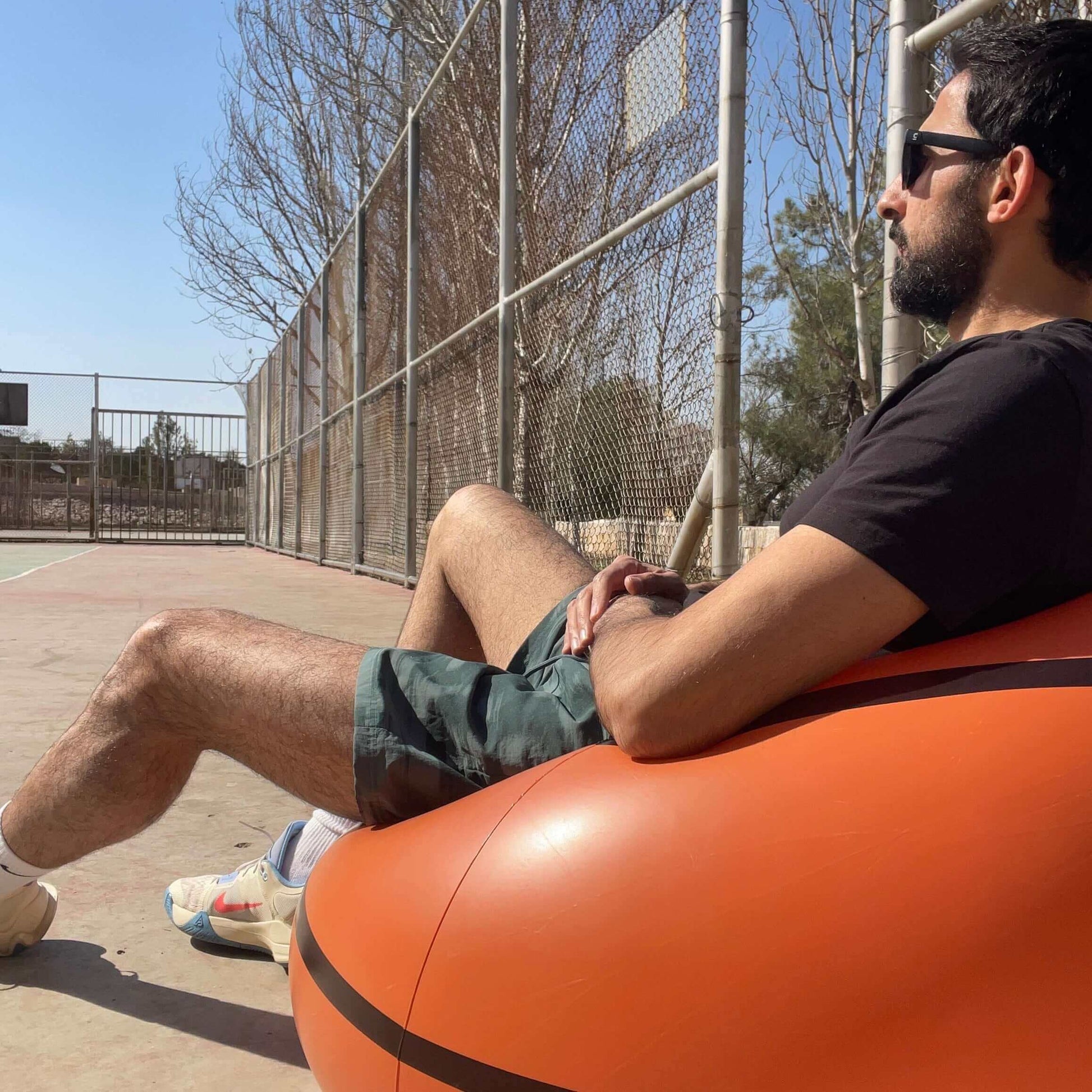 A person sitting on an Inflatable Basketball Sofa, enjoying court side comfort, wearing sunglasses and giving a thumbs up.