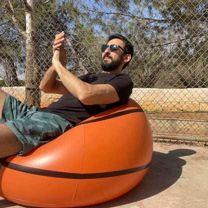 A person sitting on an Inflatable Basketball Sofa, enjoying court side comfort, wearing sunglasses and giving a thumbs up.