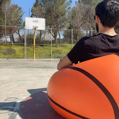 A person sitting on an Inflatable Basketball Sofa, enjoying court side comfort, wearing sunglasses and giving a thumbs up.