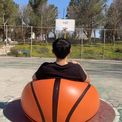 Young person relaxing in an inflatable basketball sofa at a park basketball court.