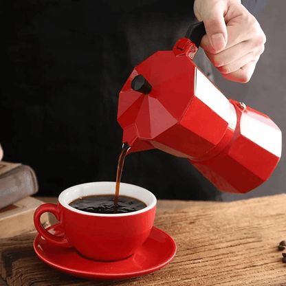 Stovetop Espresso Maker pouring coffee into a red cup on a wooden table, showcasing a traditional moka pot.