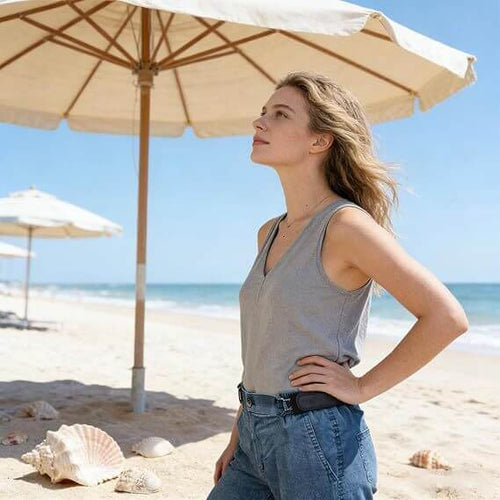 Woman wearing a casual gray tank top and high-waisted jeans on the beach under an umbrella.