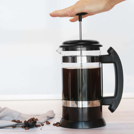 Hand pressing down on the plunger of a Glass French Press to brew coffee.