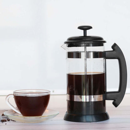 Glass French Press with freshly brewed coffee beside a clear cup on a saucer, showcasing a stylish coffee setup.