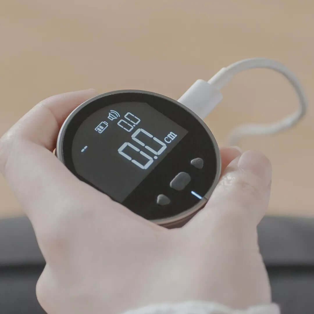 A hand holds the PrecisionCore HD High Precision Electronic Measuring Ruler Tool with a digital display showing 0.0, connected to a white charging cable. The portable device features three buttons below the screen for easy use.
