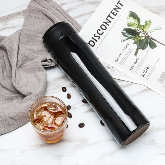 Portable Espresso Maker next to a glass of iced coffee on a marble surface.