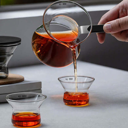 Pouring tea from a Magnetic Tea Pot into two small glass cups on a table.