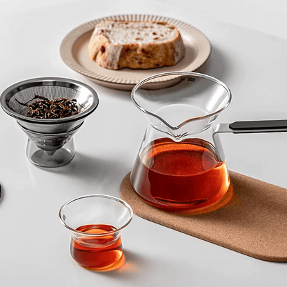 Magnetic Tea Pot brewing tea with glass infuser and a slice of cake on a table.