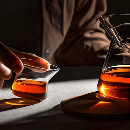 Person holding a small glass of brewed tea beside a magnetic tea pot.