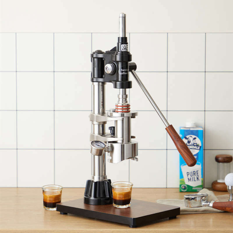 Manual Espresso Machine on a wooden base with two espresso shots and milk carton in the background.