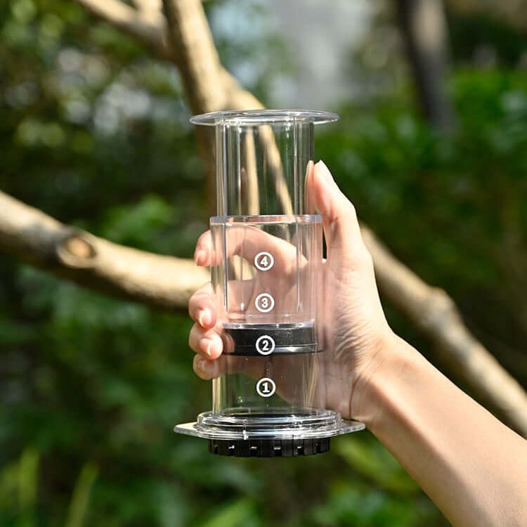 Hand holding a Portable Espresso Maker with transparent design for brewing coffee on the go.