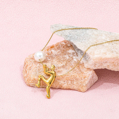 The Ambition Pearl Necklace featuring a gold figure and a centerpiece pearl, showcased on pink rocks.