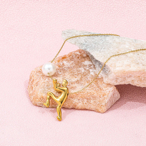 The Ambition Pearl Necklace featuring a gold figure and a centerpiece pearl, showcased on pink rocks.