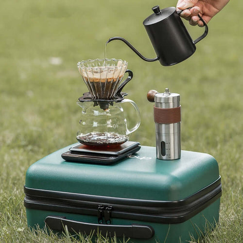 Travel coffee maker set in outdoor setting with V60 pour over kit and coffee grinder.